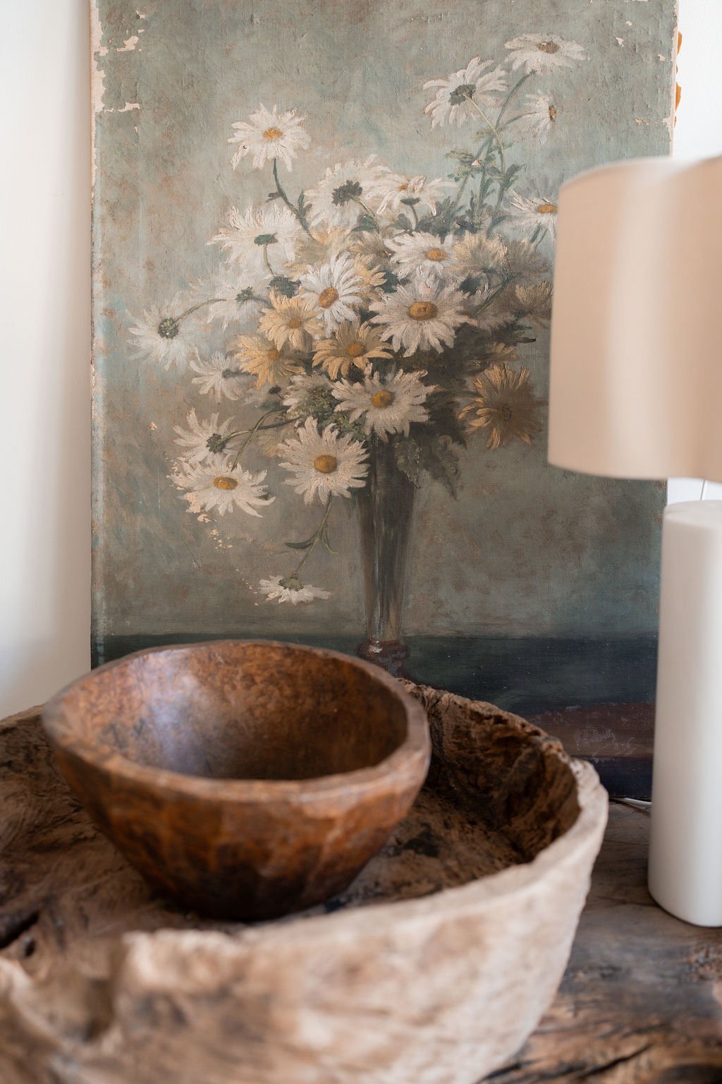 Decorative setting with a wooden bowl, woven basket, and floral painting in the background.