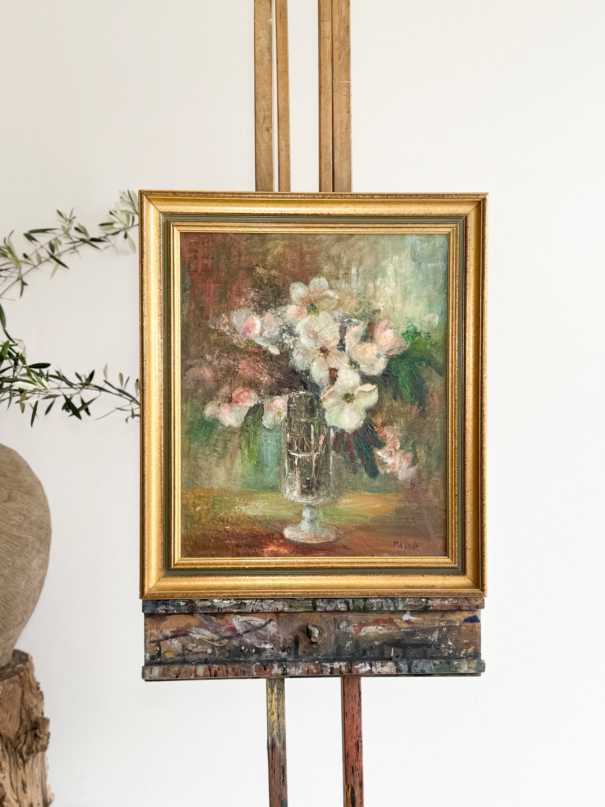 Framed painting of flowers on an easel against a white wall. Antiques, art and objects