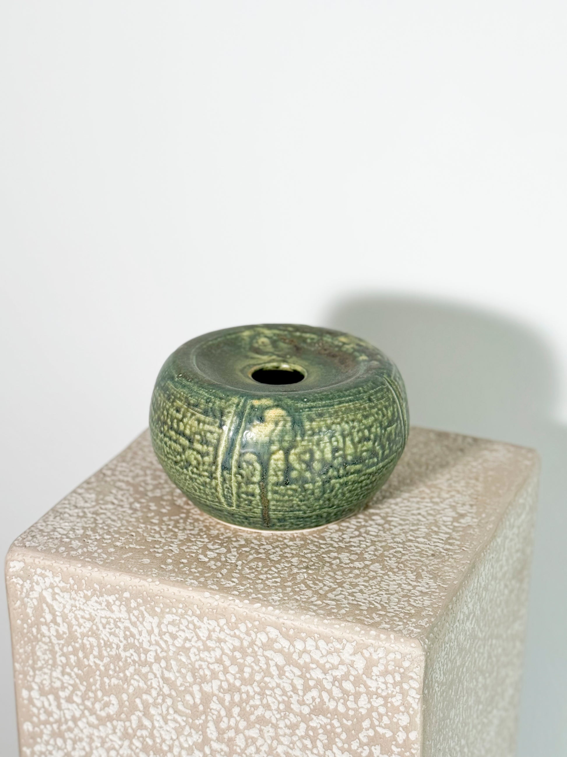 Stunning small, round ceramic vase with a green celadon glaze and a textured chattered pattern.