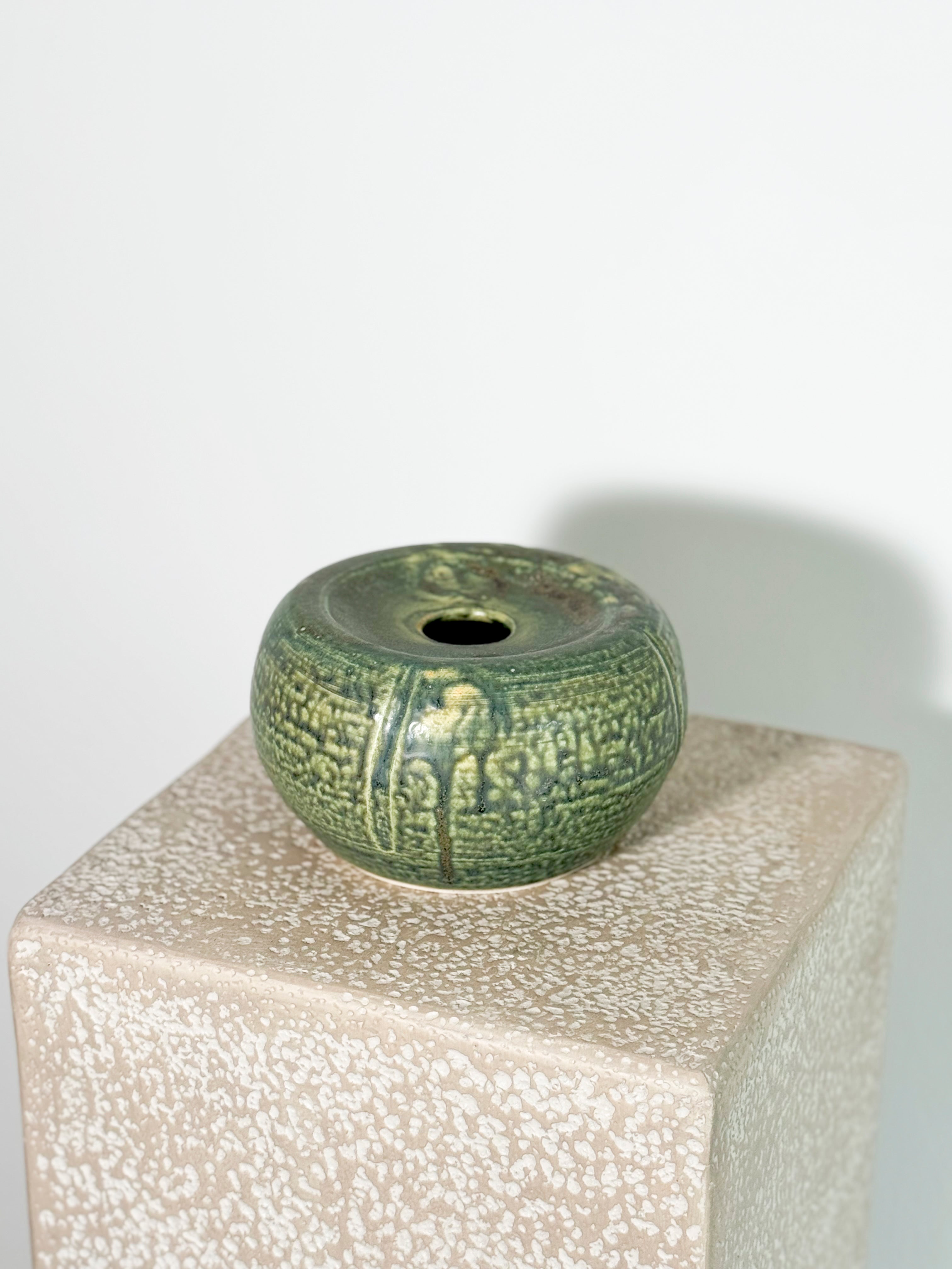 Stunning small, round ceramic vase with a green celadon glaze and a textured chattered pattern.