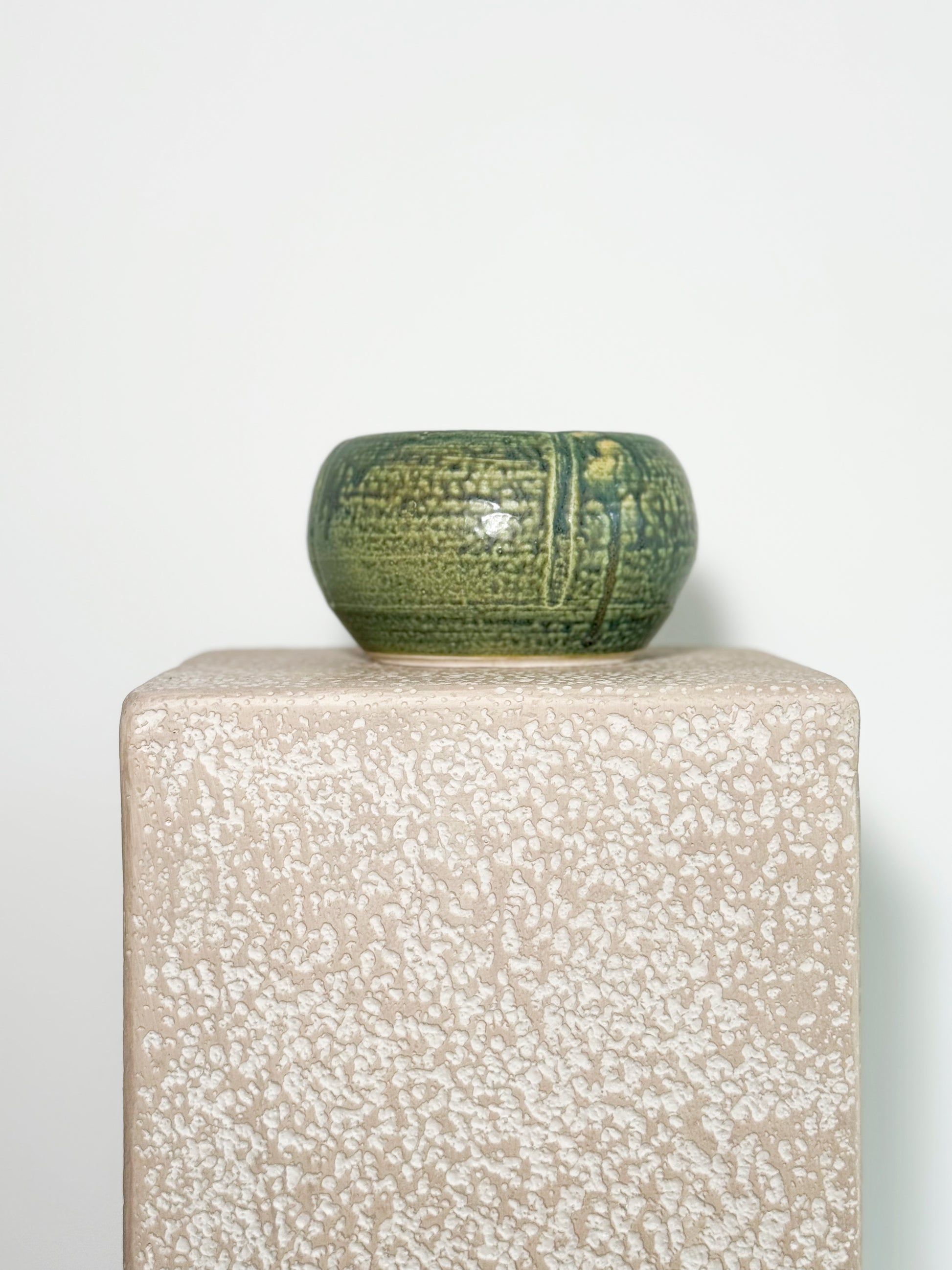 Stunning small, round ceramic vase with a green celadon glaze and a textured chattered pattern.