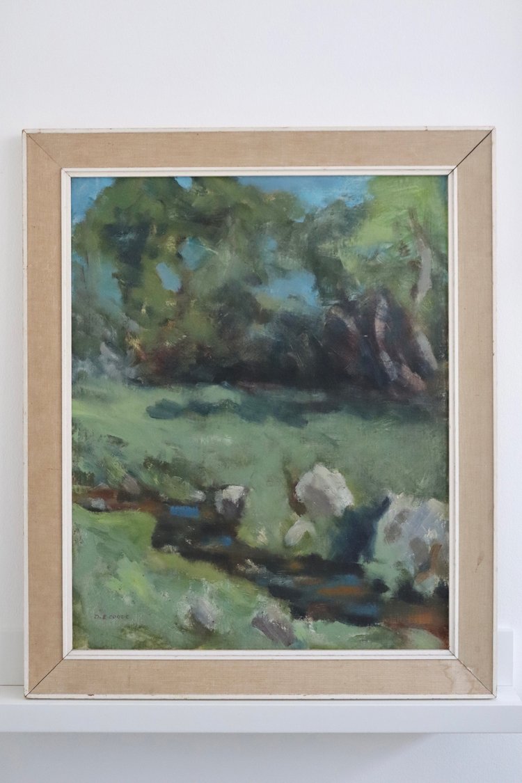 Framed painting of a landscape with trees and a stream on a white wall