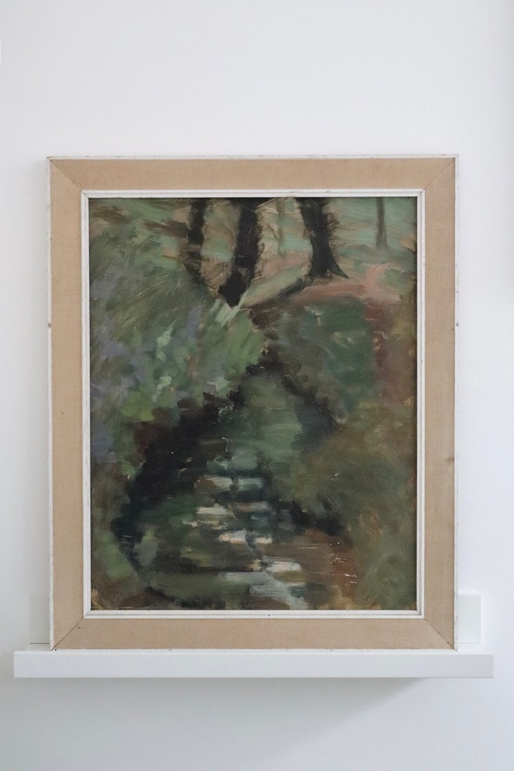 Framed painting of a natural scene with green and brown tones on a white wall.
