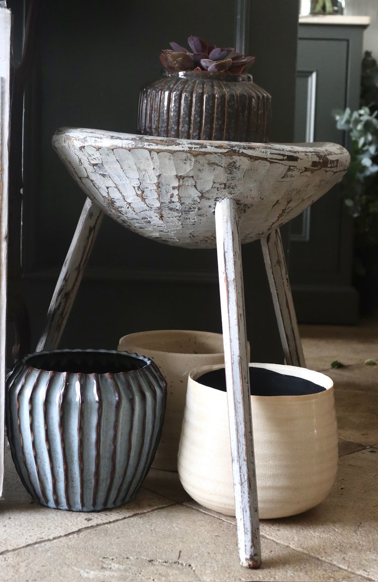 Decorative stool with rustic finish and ceramic pots on a wooden floor.