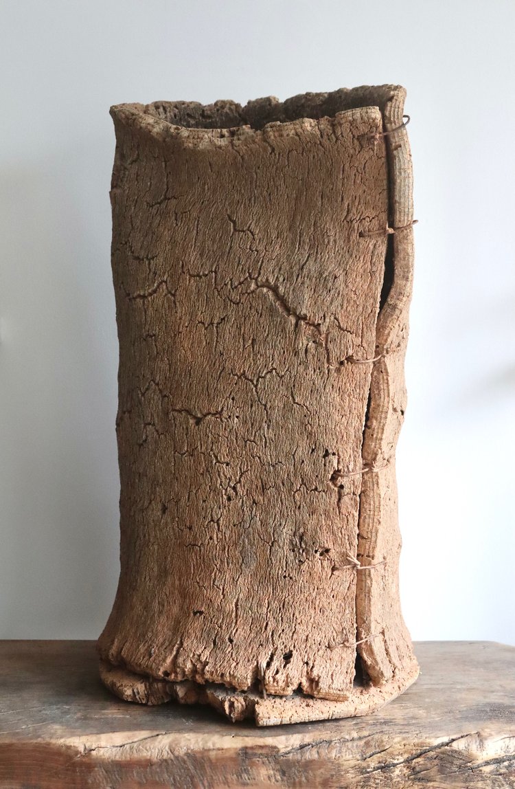 Textured brown vase on a wooden surface with a light gray background