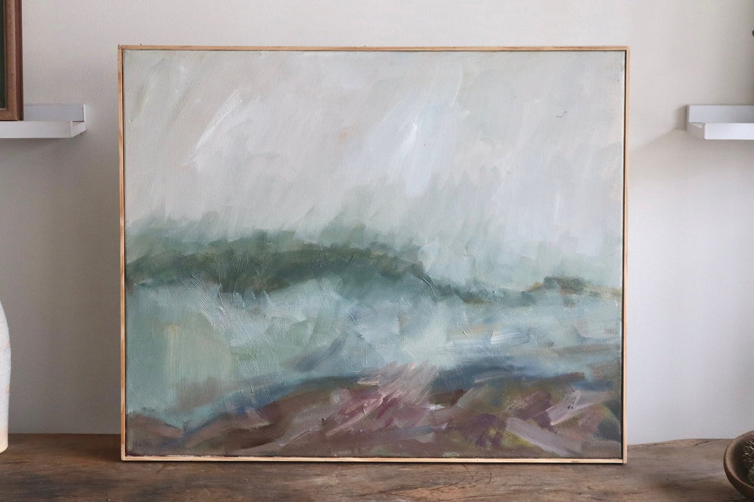Abstract painting in a gold frame on a wooden surface with a neutral background