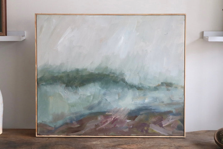 Abstract painting in a gold frame on a wooden surface with a neutral background