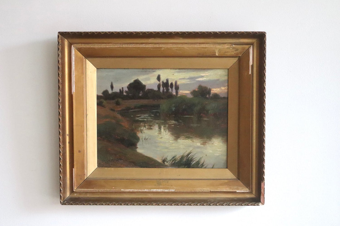 Framed painting of a landscape with a river and trees on a white wall