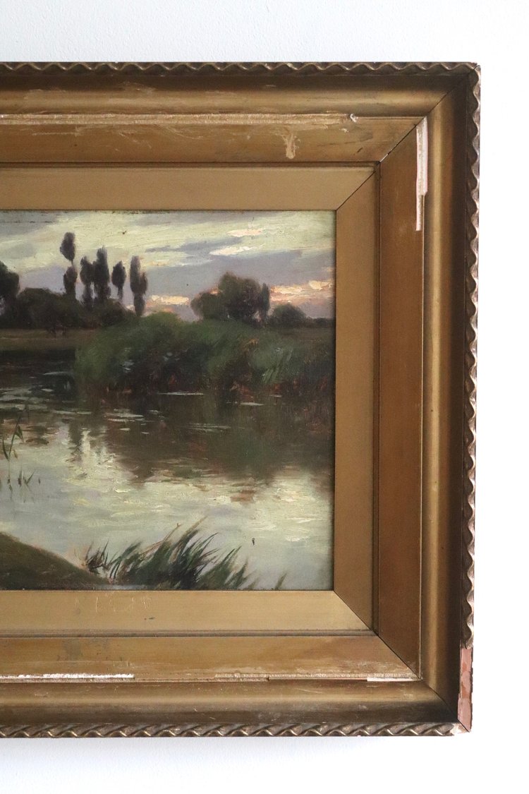 Painting of a landscape with trees and water in a gold frame.