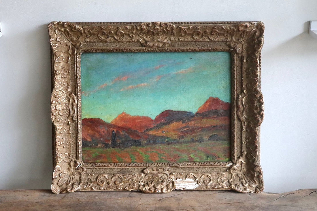 Framed painting of a landscape with mountains on a wooden surface.