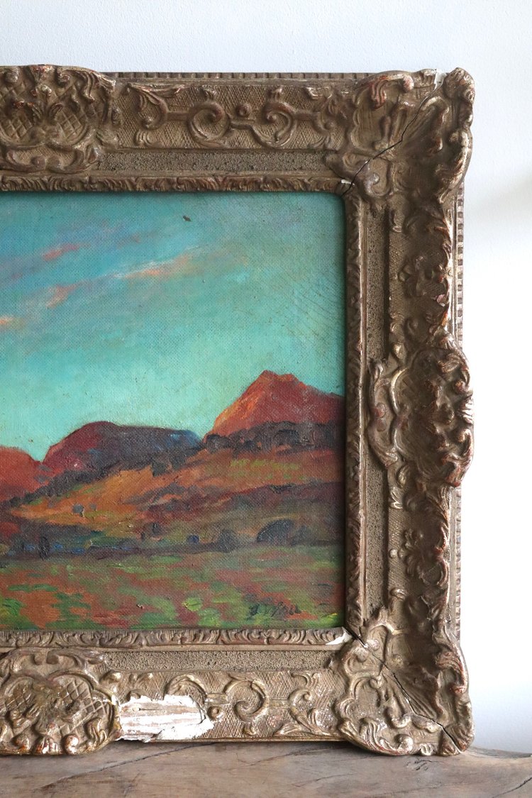 Vintage landscape painting in an ornate gold frame on a white wall.