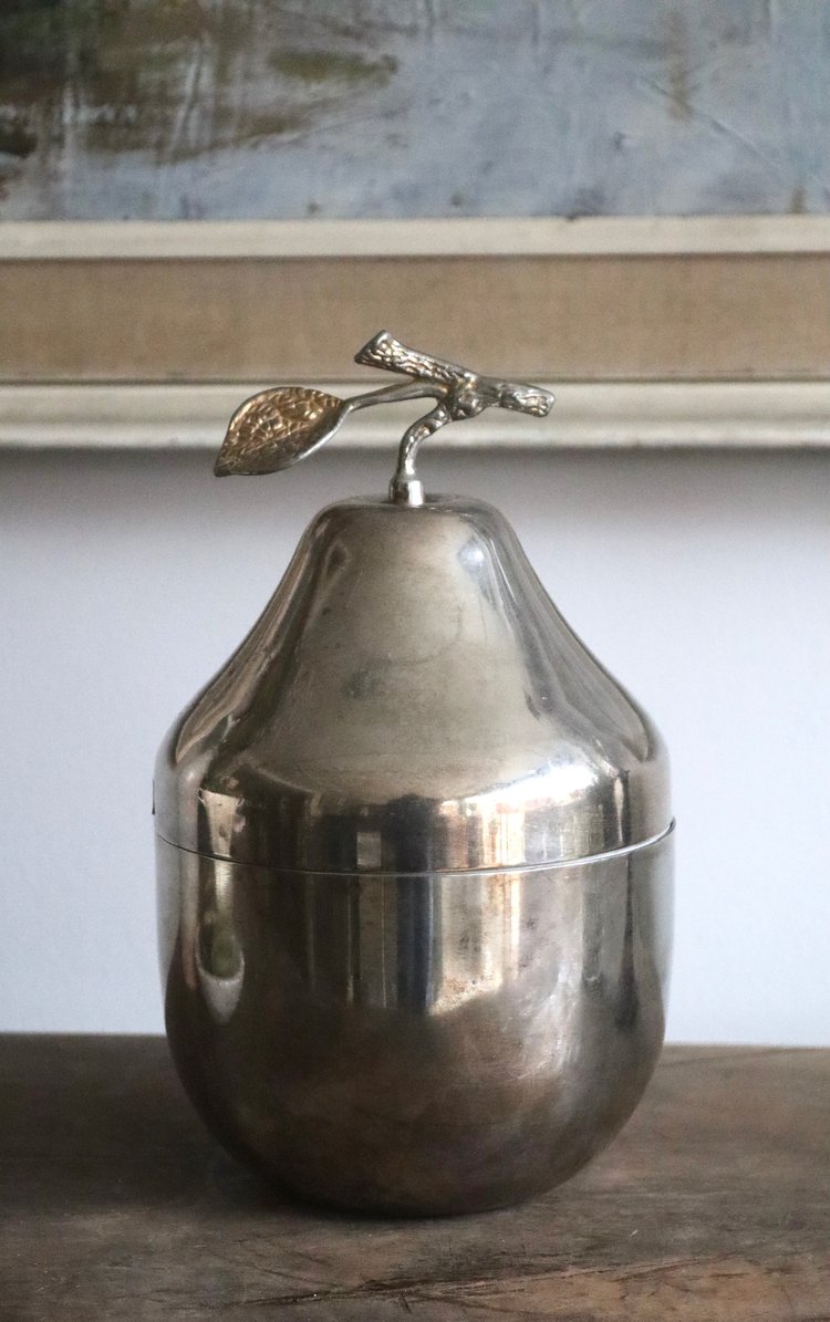 Metallic pear-shaped container with a leaf finial on a wooden surface.