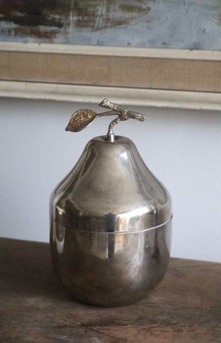 Metallic pear-shaped container with a leaf on top, placed on a wooden surface.