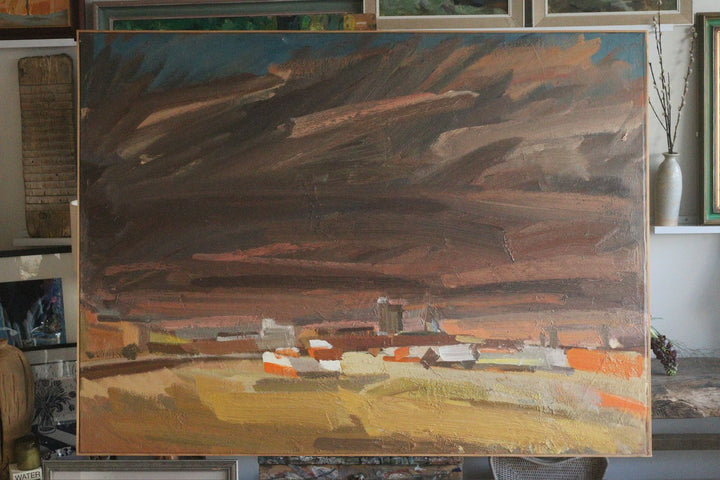 Painting of a landscape with fields and buildings, held by an artist.