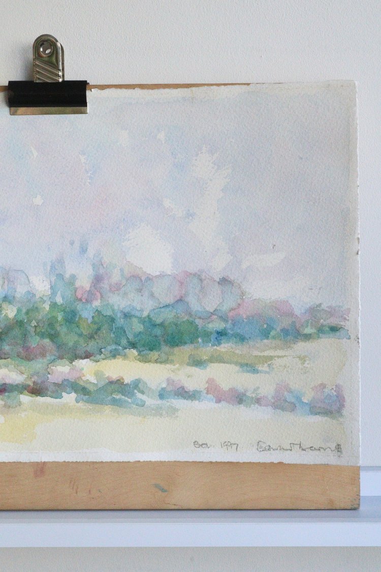 Watercolor landscape painting clipped to a white board with a signature at the bottom right corner.