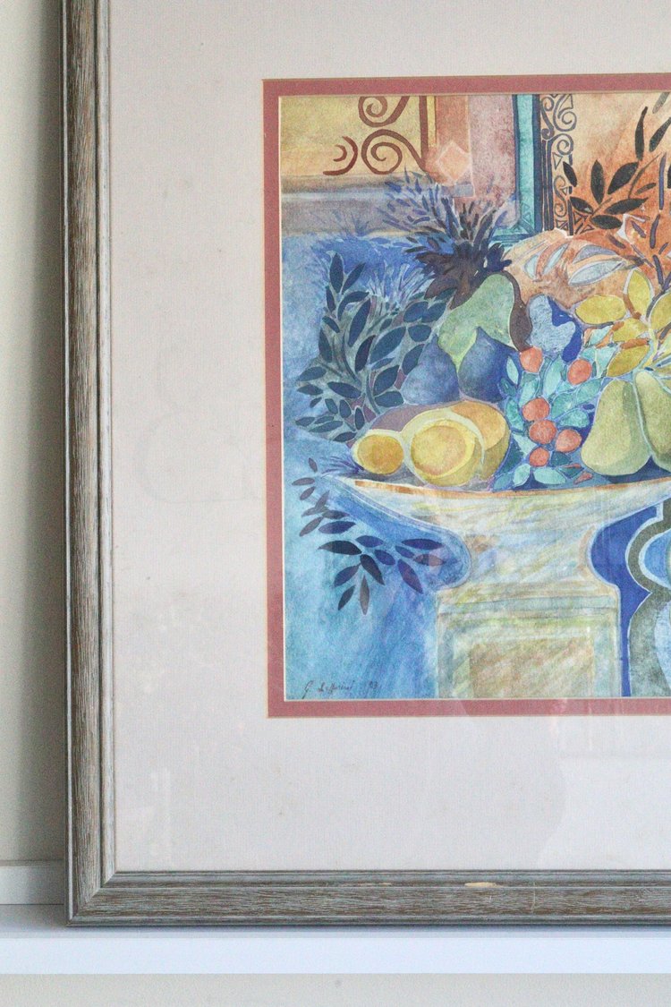 Framed watercolor painting of a still life scene with fruits and flowers on a table.
