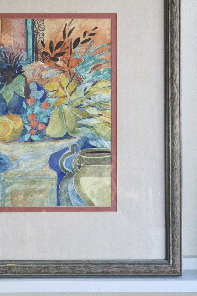 Framed artwork of a still life scene with flowers and a pot on a white wall.