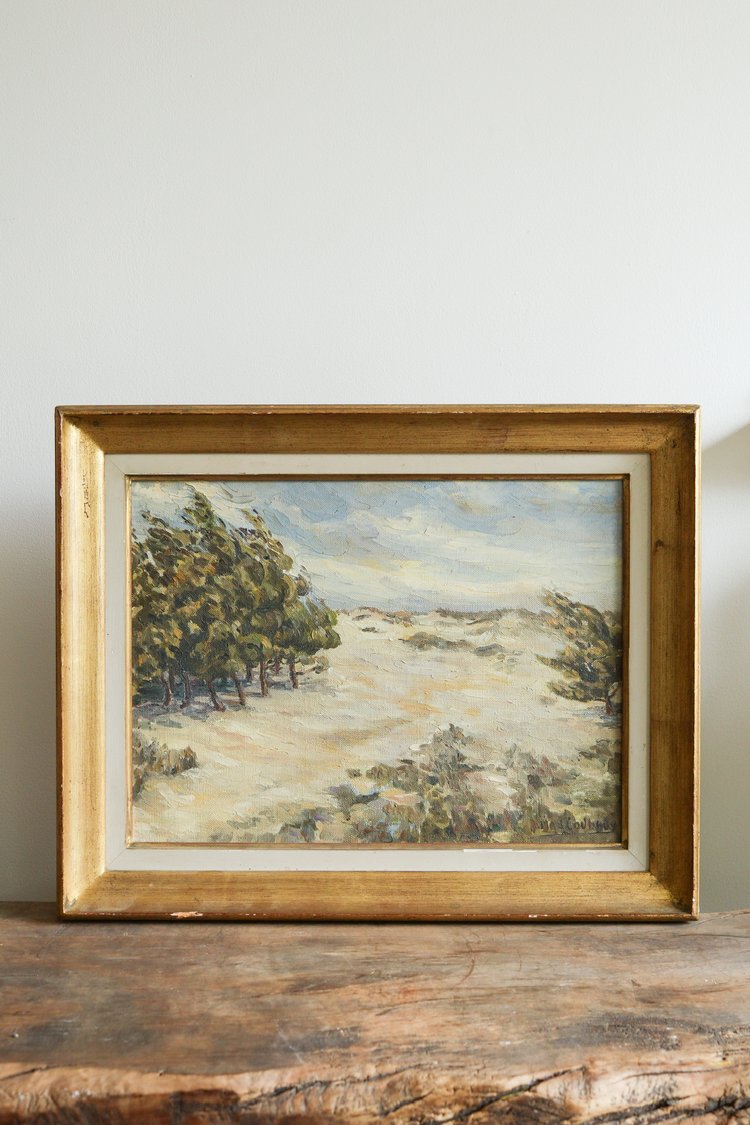 Framed painting of a landscape with trees on a wooden surface