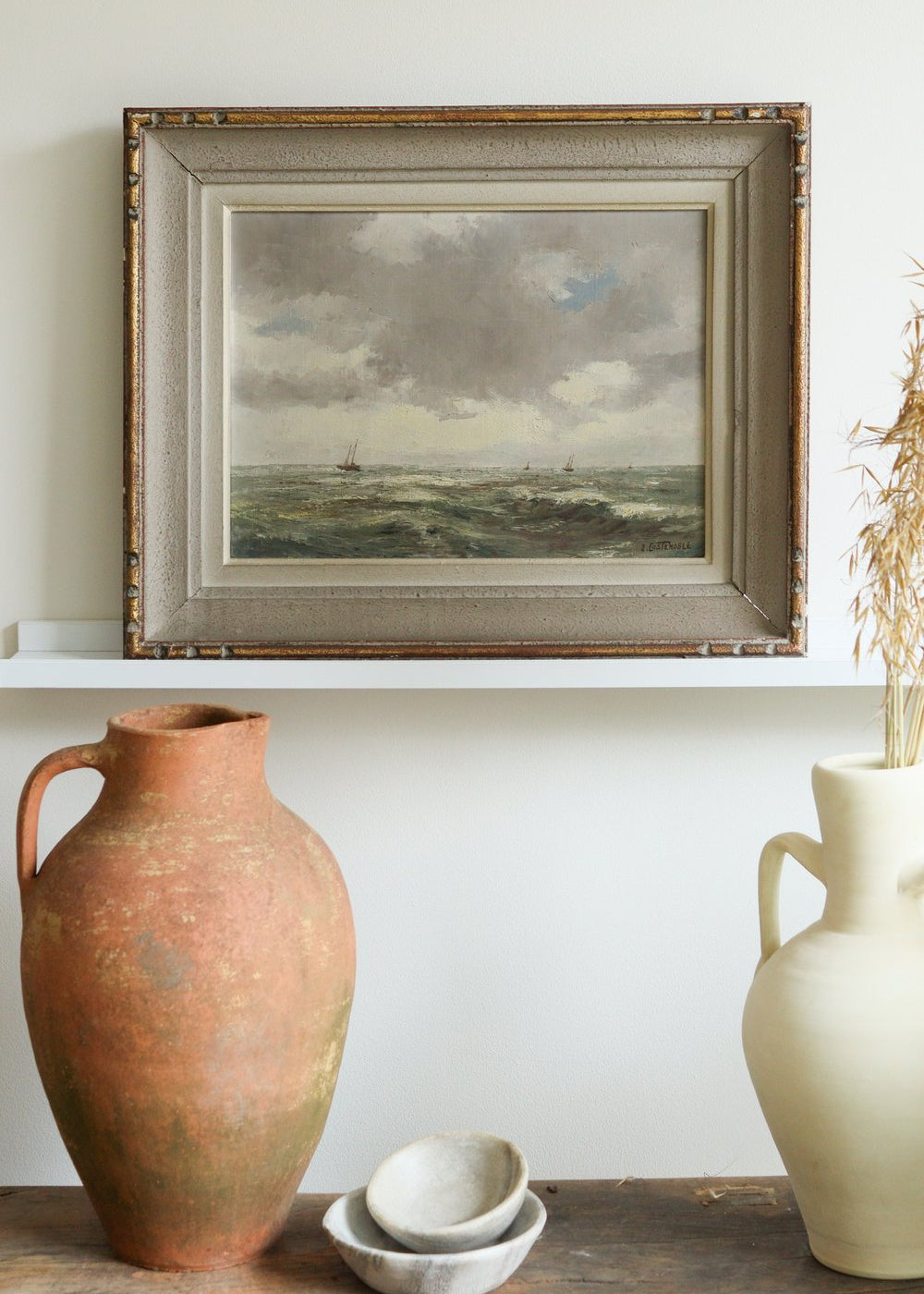 Two ceramic jars on a wooden surface with a framed landscape painting above.