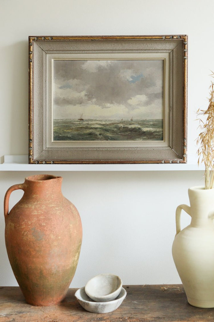 Framed landscape painting above two ceramic jars on a wooden surface.