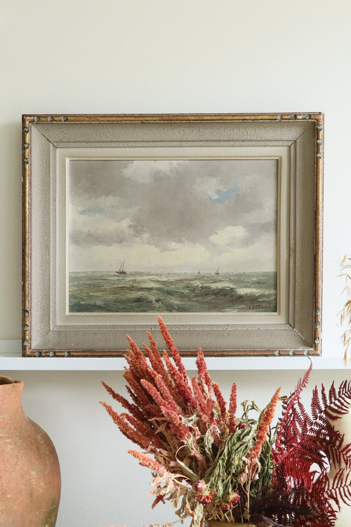Framed painting of a landscape with a cloudy sky, placed above a shelf with decorative plants.