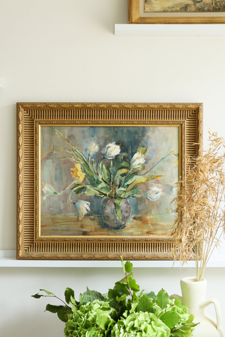 Framed painting of flowers on a white wall with greenery below