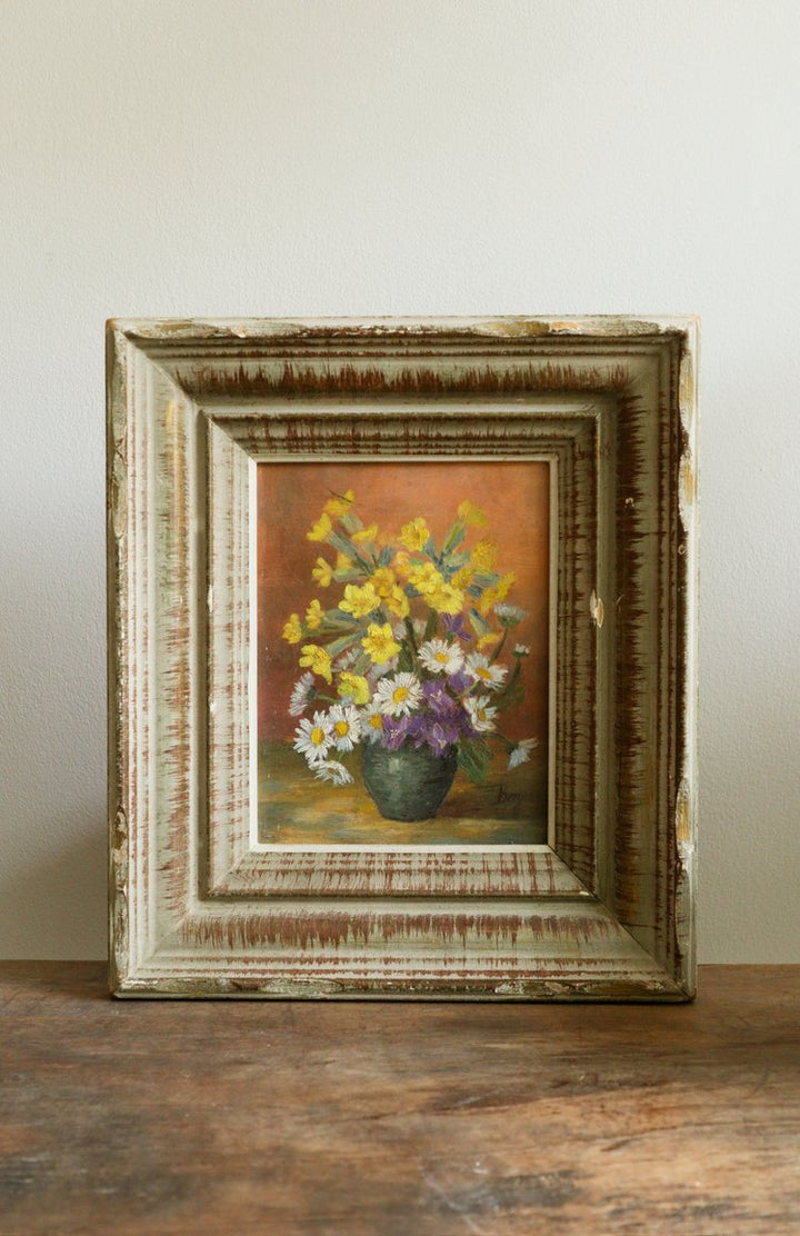 Framed painting of flowers on a wooden surface with a neutral background