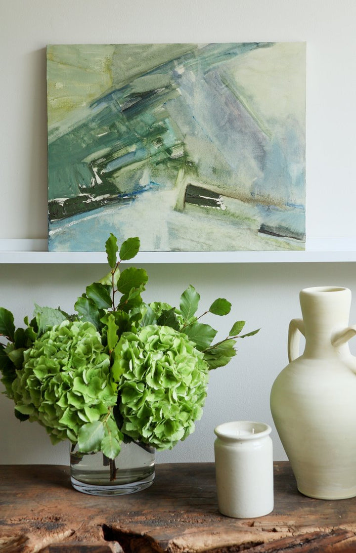 Decorative setup with green flowers, a vase, and abstract painting on a shelf.