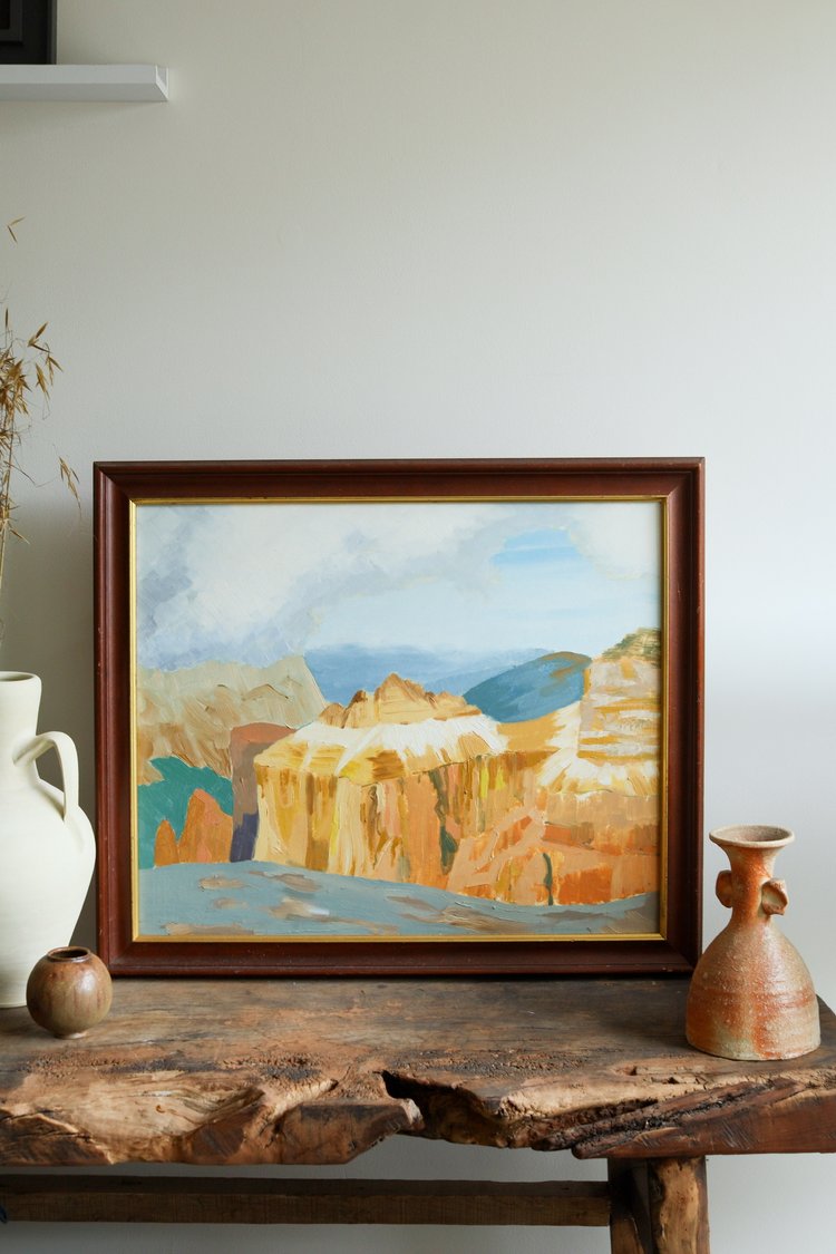 Framed landscape painting on a wooden table with decorative items.