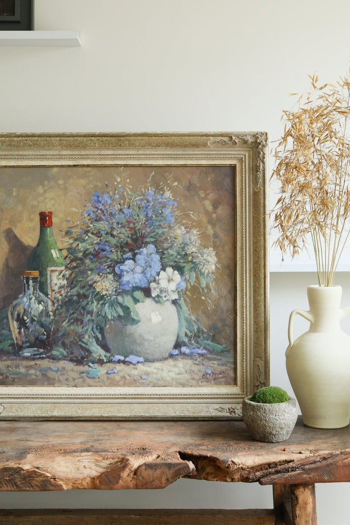 Framed still life painting with flowers and bottles on a wooden table.