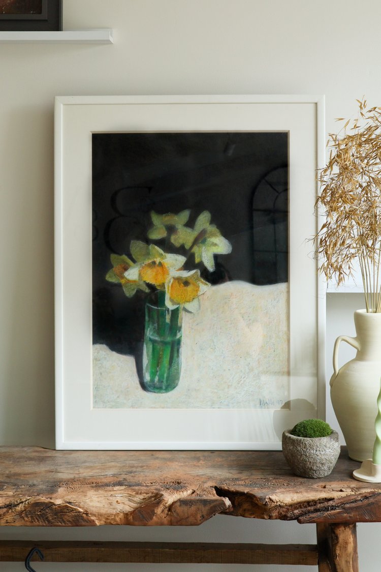 Framed artwork of flowers on a wooden table with decorative items.