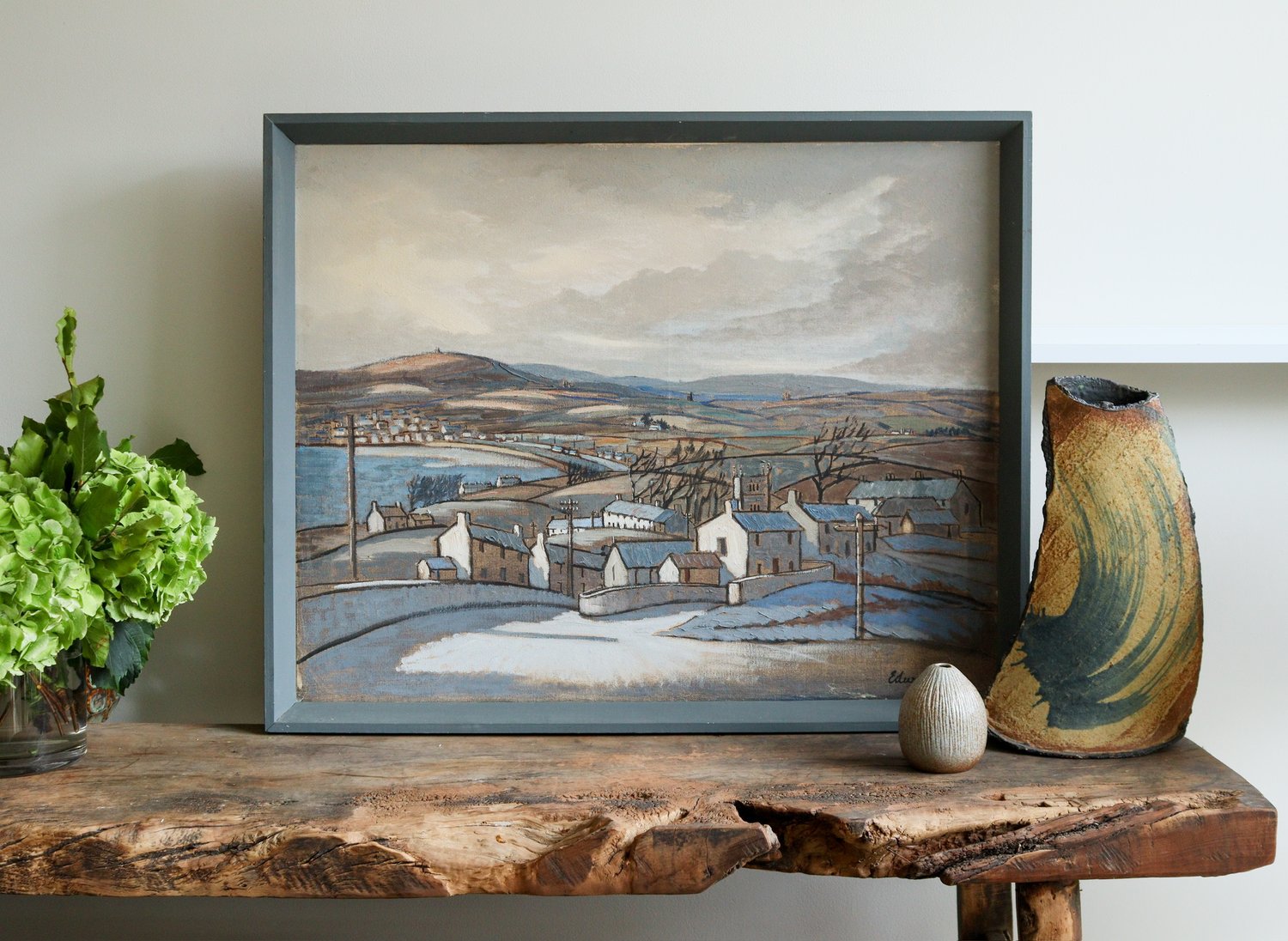 Framed landscape painting on a wooden surface with decorative items.