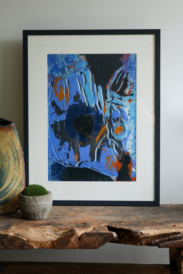 Framed abstract artwork on a wooden surface with a neutral background