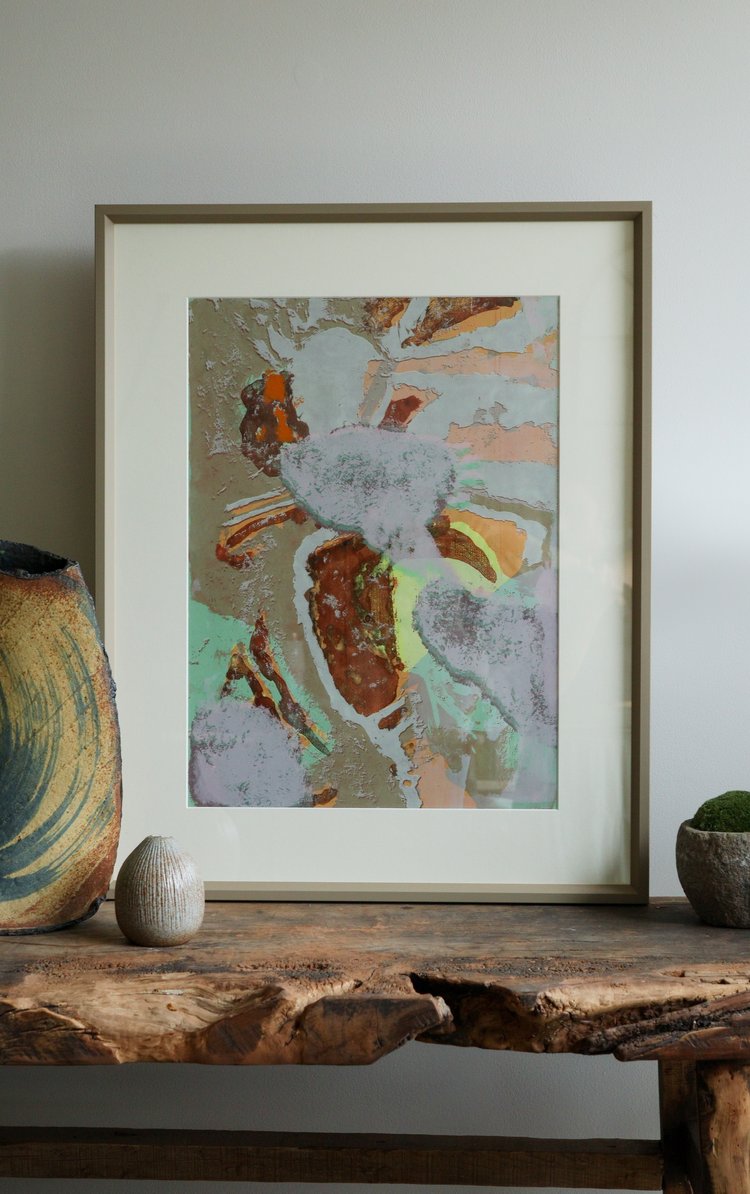 Framed abstract art piece on a wooden surface with decorative items.