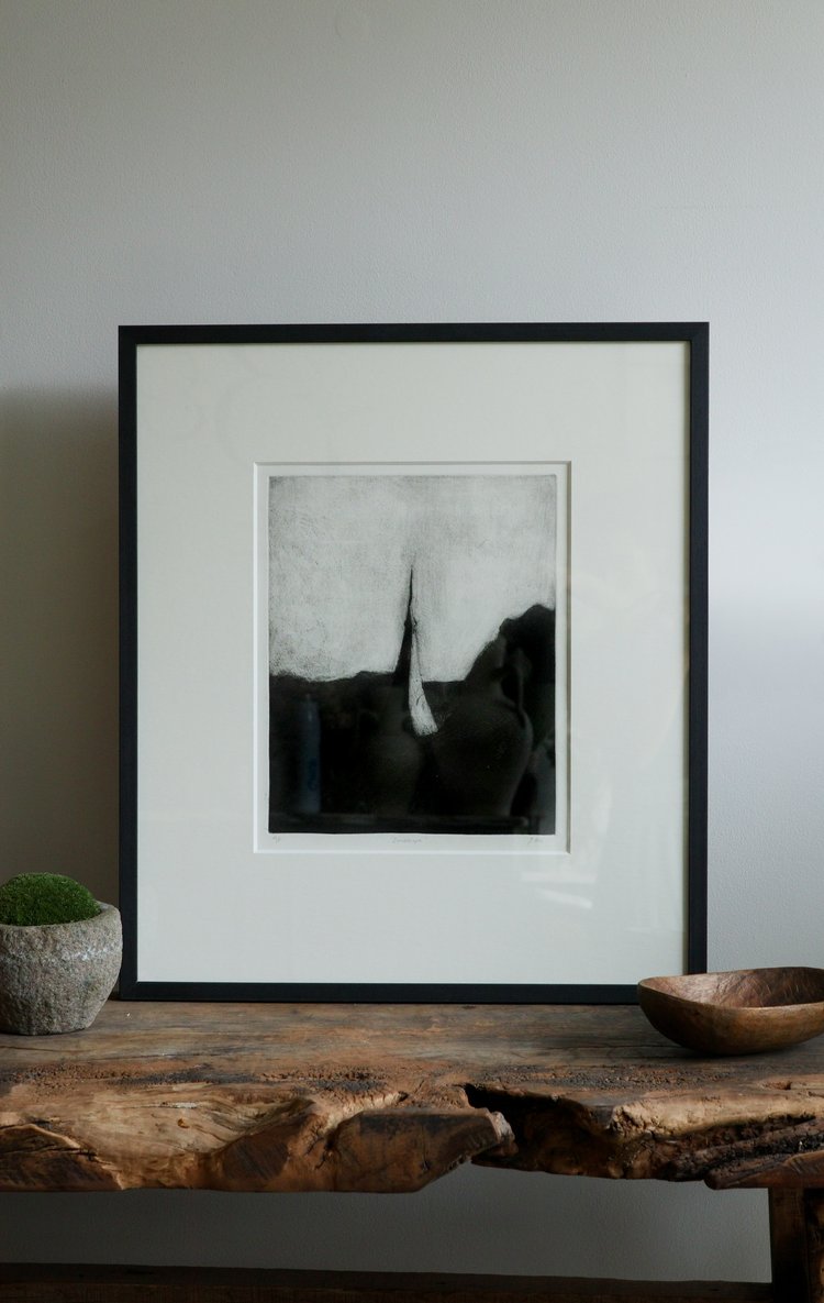 Framed black and white photograph on a wooden surface with a plant and bowl.