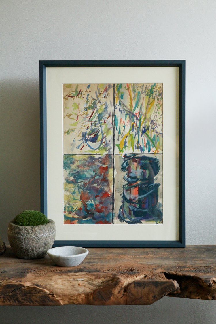 Framed abstract artwork on a wooden surface with a plant and bowl.