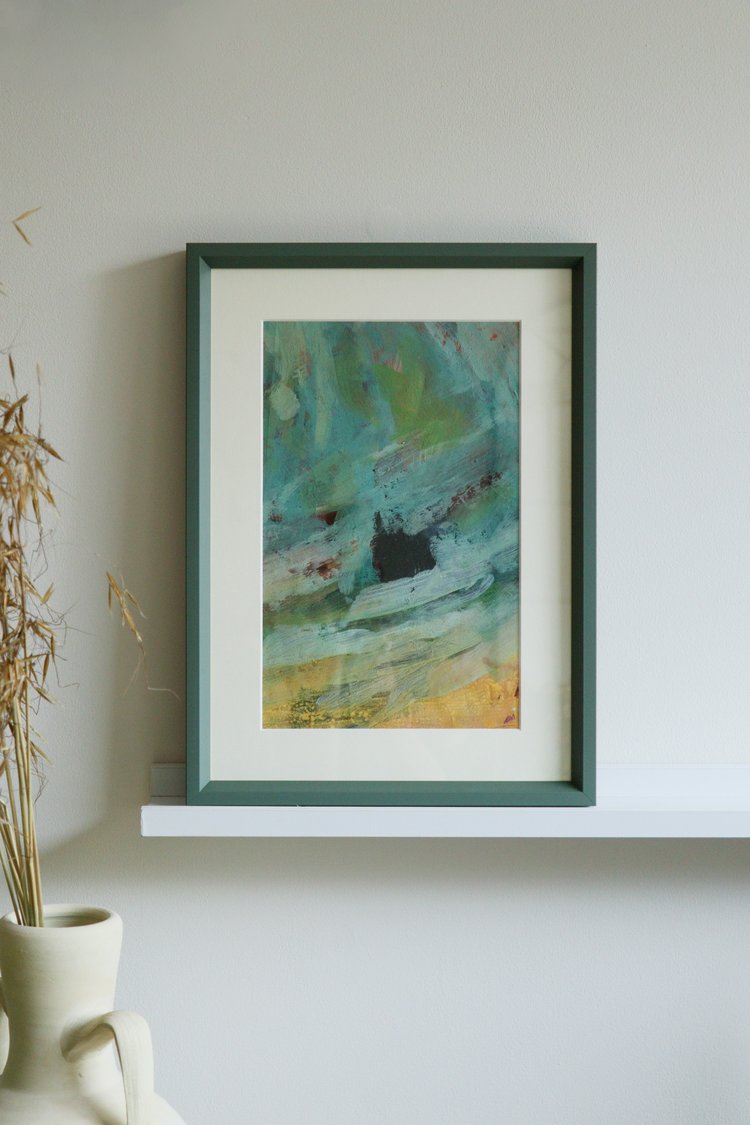 Framed abstract painting on a white wall with a vase and plant to the left.