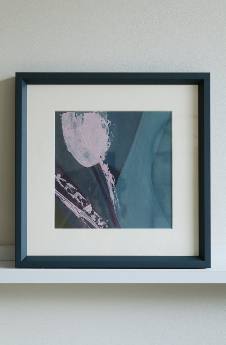 Framed abstract artwork with a blue and pink color scheme on a white shelf.