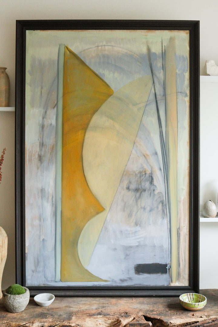 Abstract art piece in a black frame on a wooden surface with decorative items.