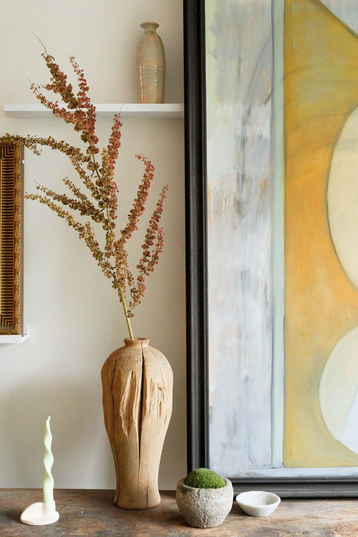 Decorative setting with a wooden vase, dried plants, and a painting in a room.