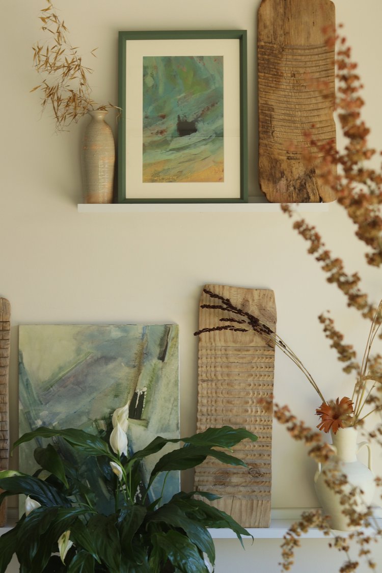 Decorative wall with framed artwork, a plant, and dried flowers.