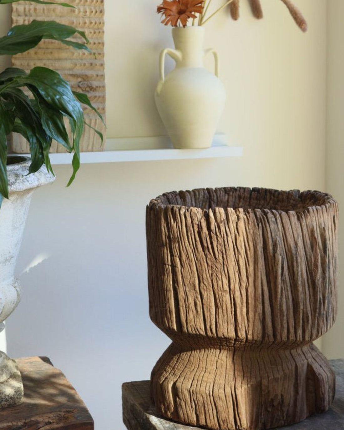 Decorative wooden planter with a white vase and plant on a shelf in the background.