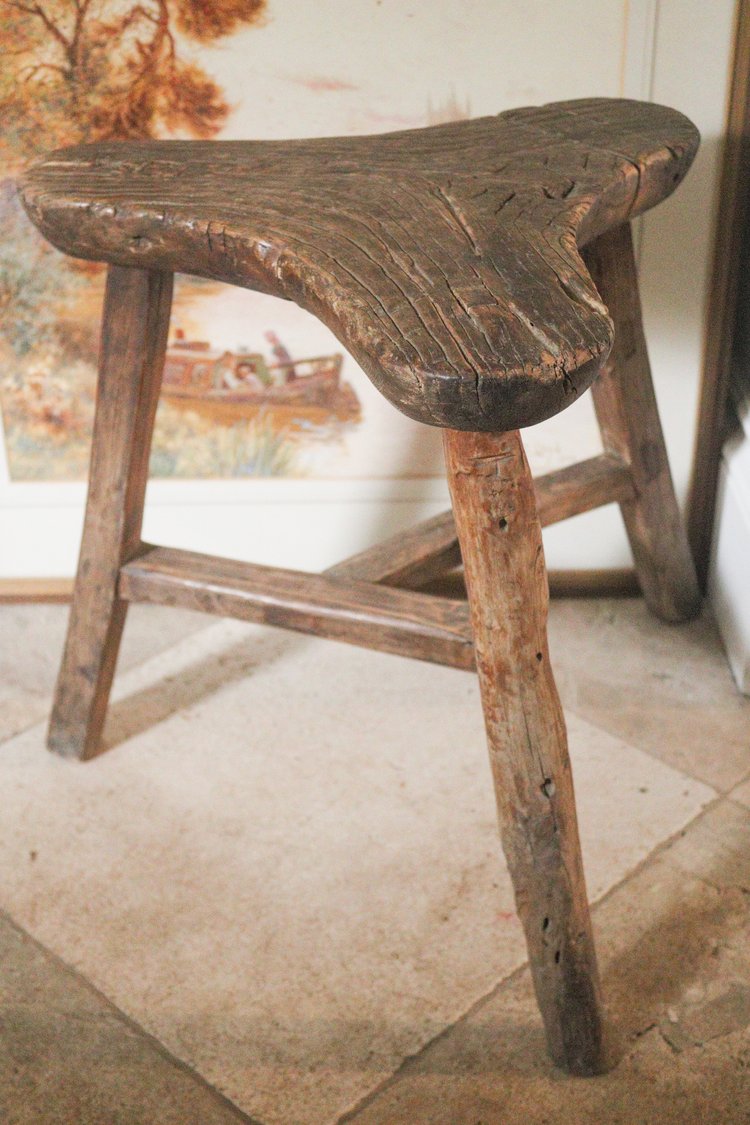 Vintage wooden stool on a stone floor with a blurred painting in the background
