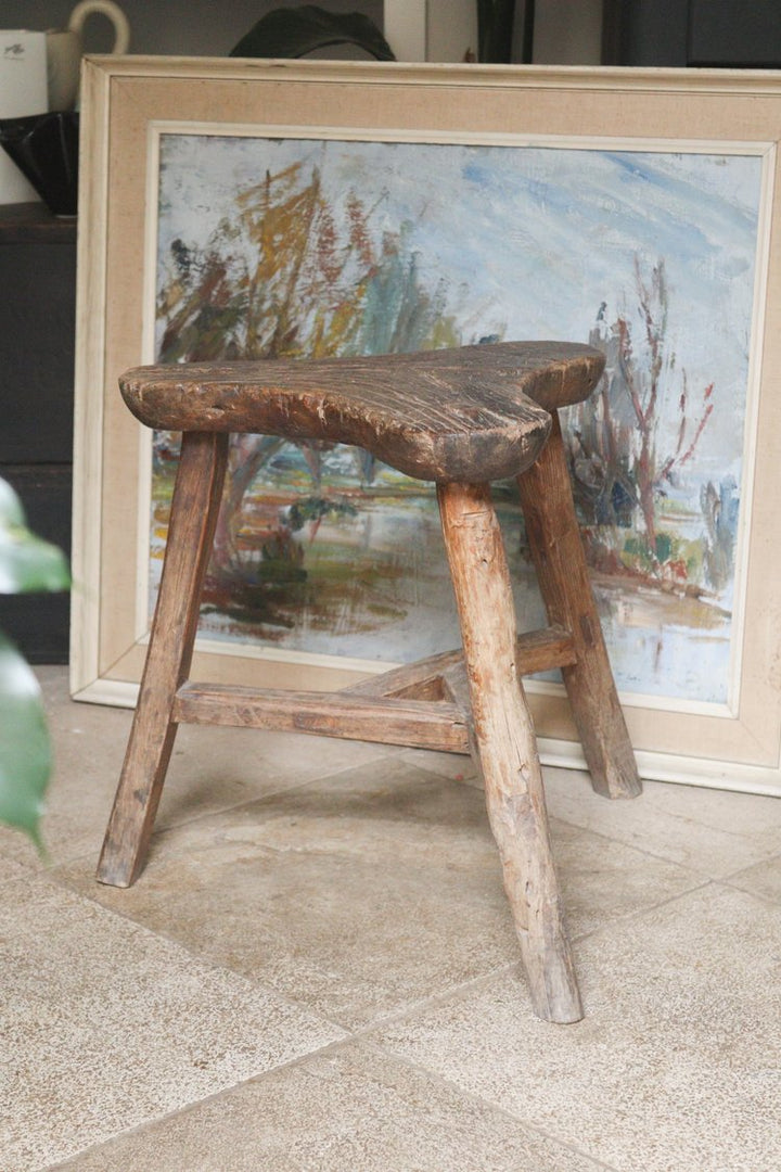 Wooden stool in front of a framed painting on a textured surface