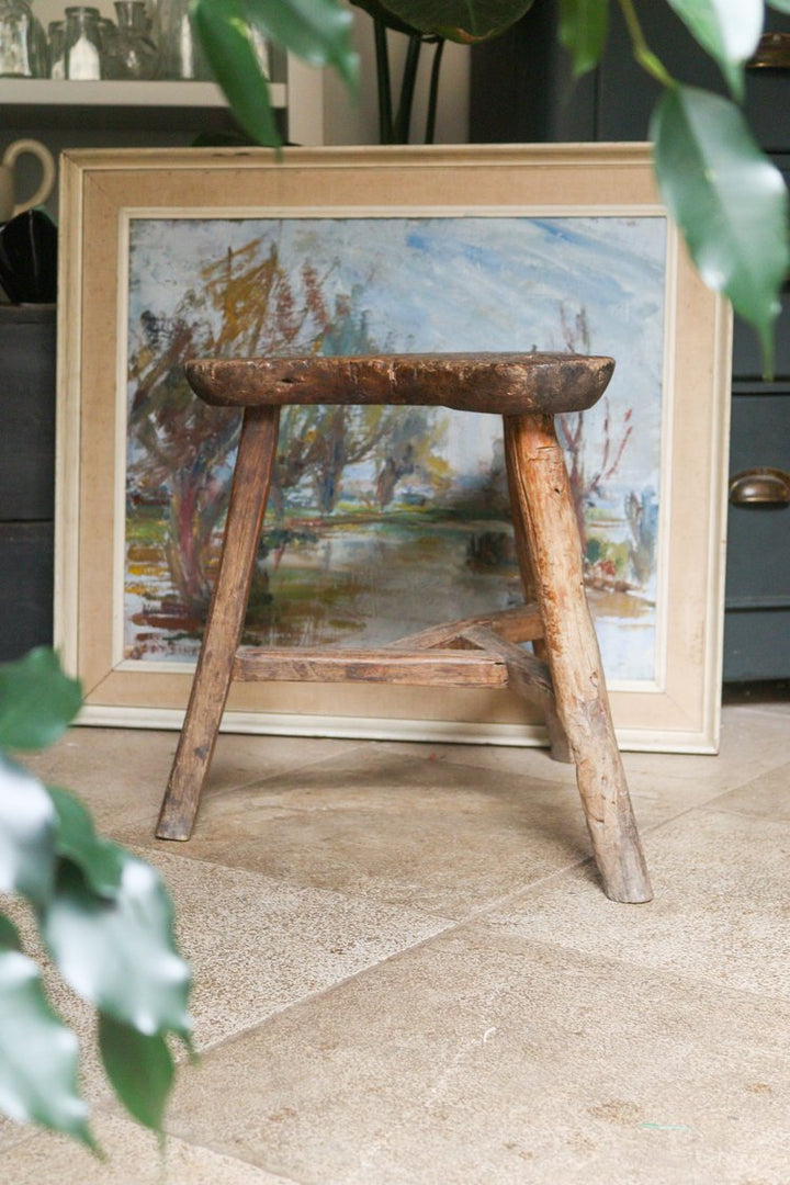 Wooden stool in front of a framed painting on a stone floor