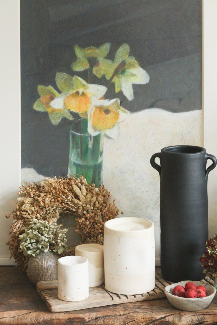 Decorative setting with candles, flowers, and a black vase on a wooden surface.
