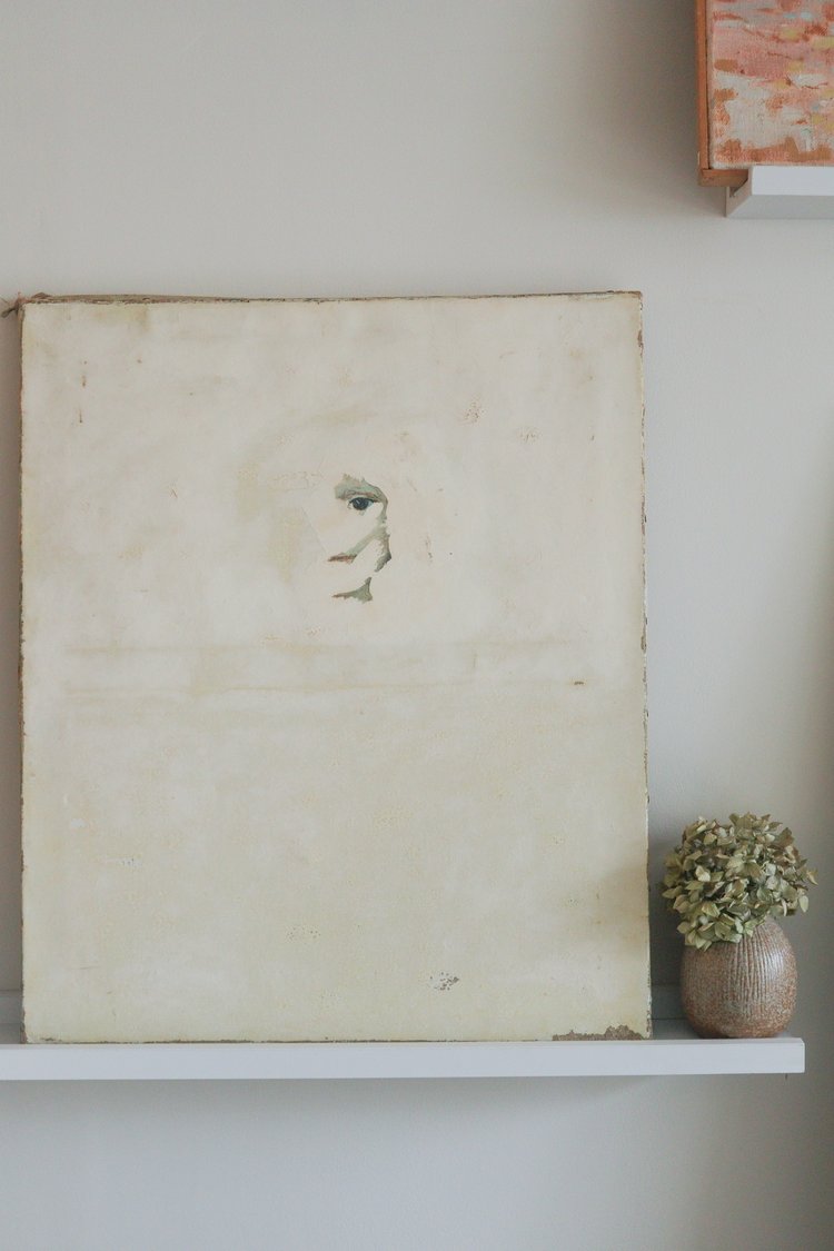 Vintage painting on a white shelf with a small plant against a light wall.