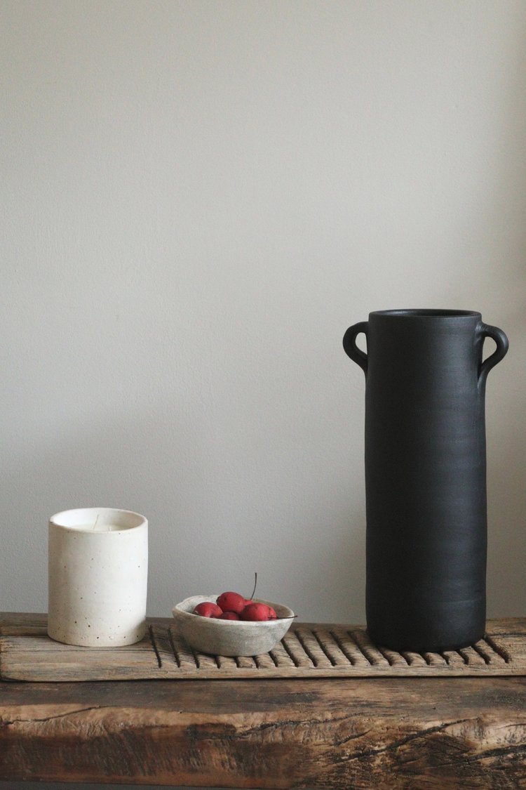 Black vase and white ceramic items on a wooden surface with a neutral background