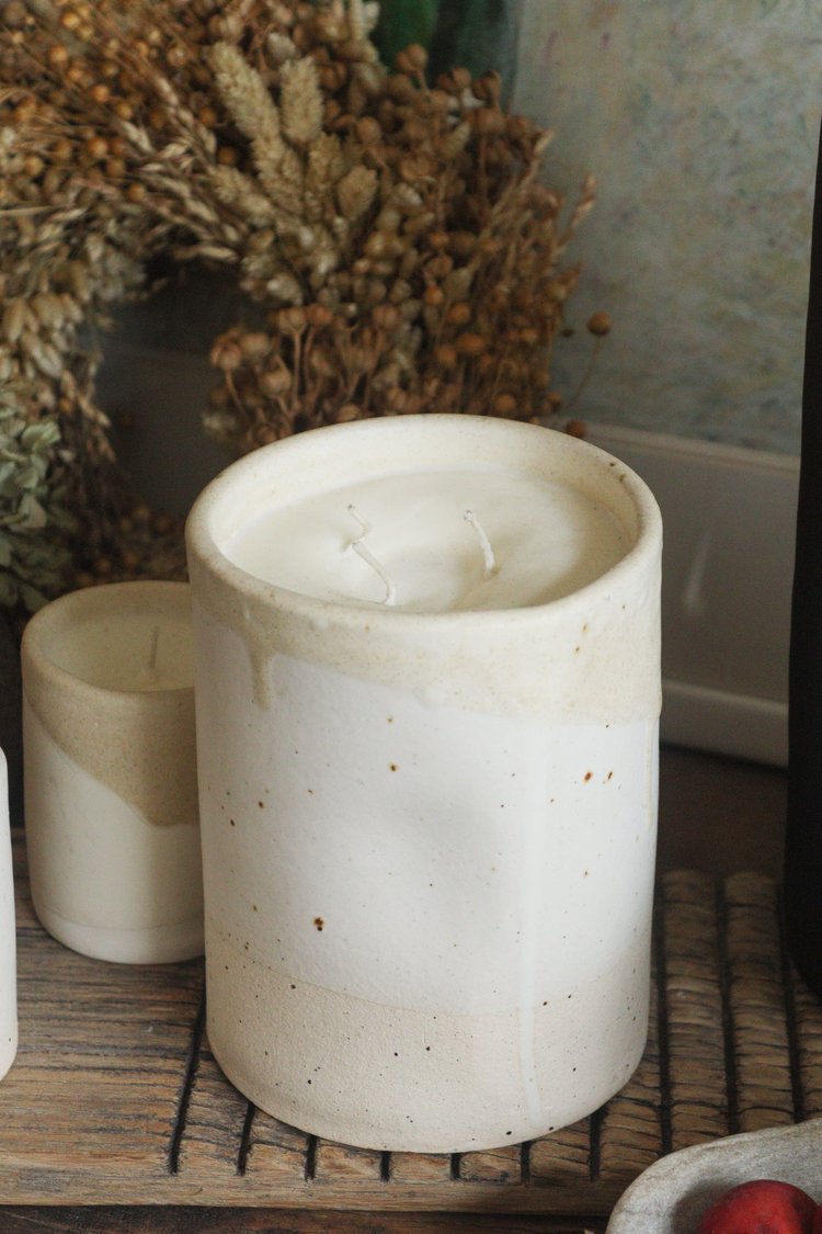 White ceramic candle on a wooden surface with decorative elements in the background