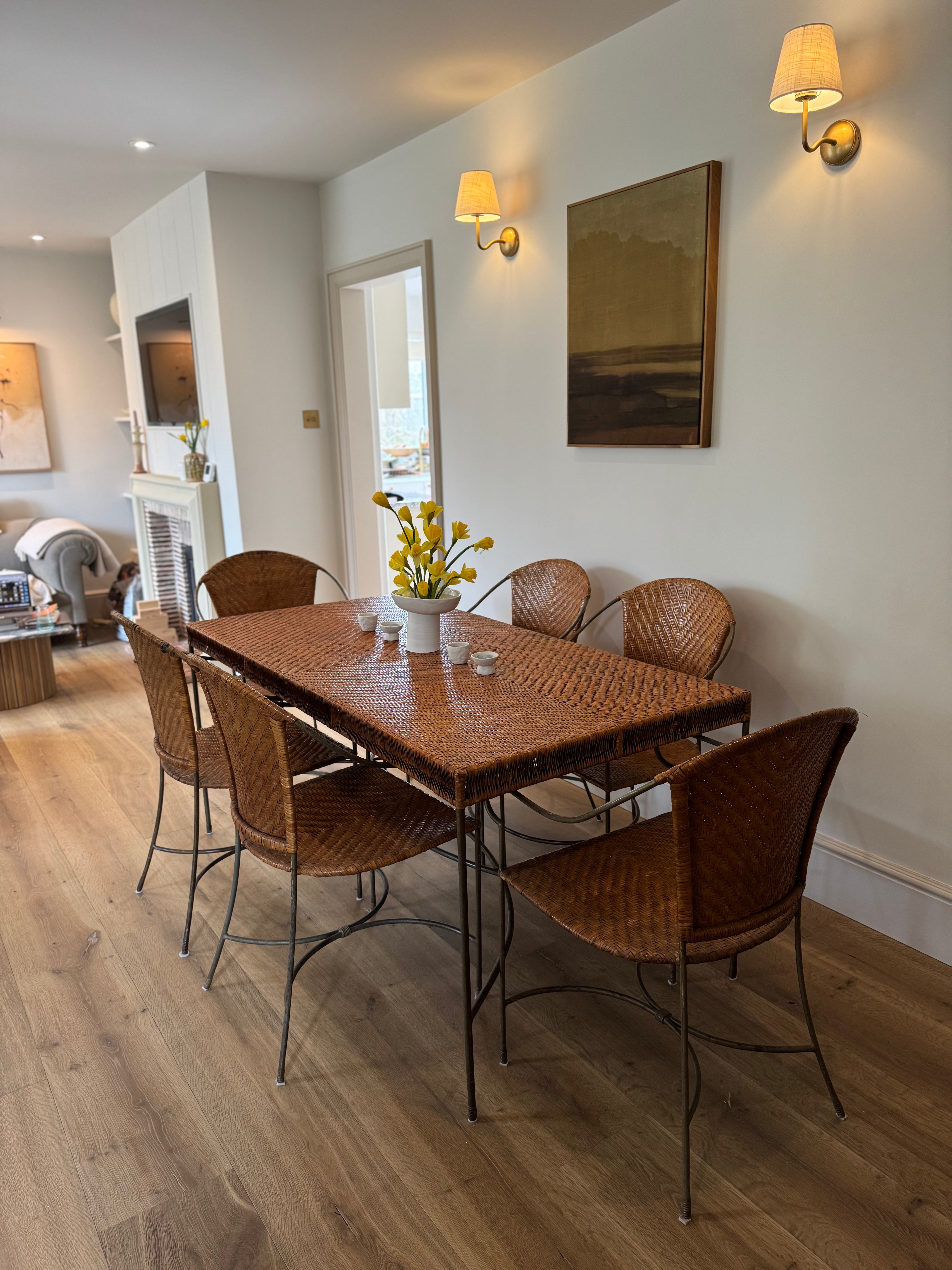 A beautifully proportioned woven rattan dining set, combining warmth, texture and sculptural metalwork in perfect balance. The rectangular table features a tightly woven herringbone rattan top in a rich honeyed tone, framed by slender dark metal legs with elegant stretchers that give the piece a light, architectural feel.